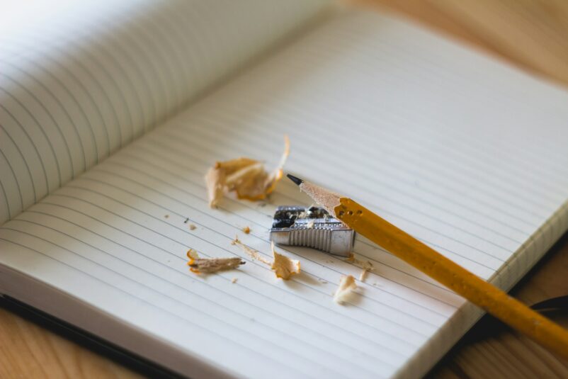 Pencil, just sharpened, resting on a blank notebook.